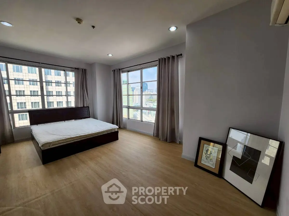 Spacious bedroom with large windows offering city views, featuring modern decor and natural light.