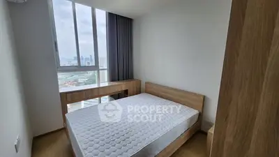 Modern bedroom with large window and wooden furniture, offering a serene city view.