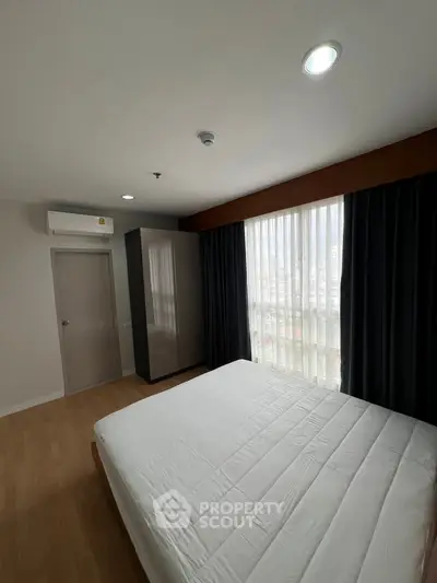 Spacious bedroom with large window and modern furnishings in a stylish apartment.