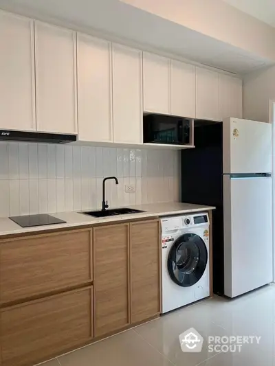 Modern kitchen with sleek cabinets, washing machine, and fridge in a stylish apartment.