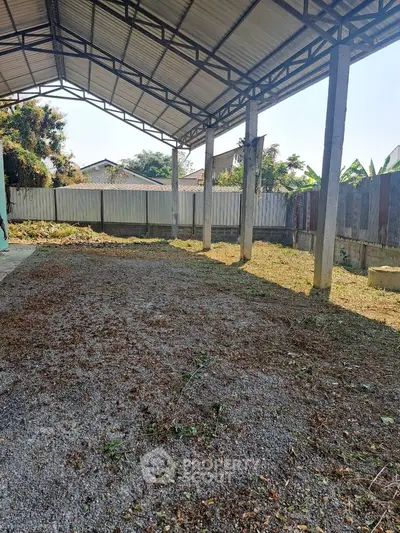 Spacious outdoor area with covered structure, ideal for parking or storage, featuring a metal roof and gravel ground.