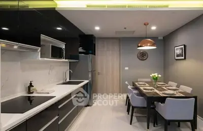 Modern kitchen with sleek black cabinets and dining area, featuring elegant lighting and contemporary decor.