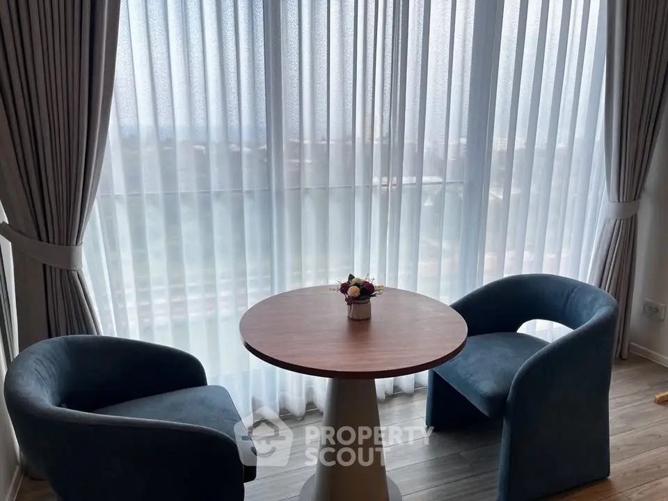 Cozy seating area with round table and chairs by large window with scenic view.