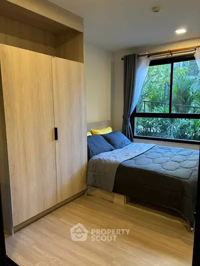 Cozy bedroom with large window and wooden wardrobe, perfect for relaxation.