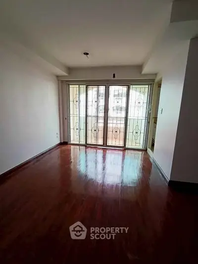 Spacious empty living room with polished wooden floors and large windows.