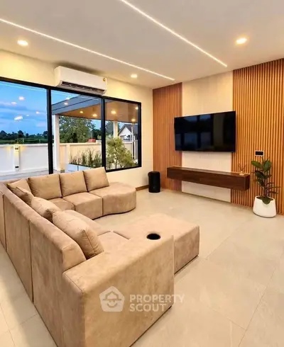 Modern living room with large sectional sofa and wall-mounted TV, featuring floor-to-ceiling windows and stylish decor.