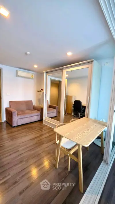 Modern living room with wooden flooring, mirrored wardrobe, and cozy seating area.