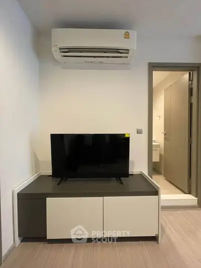 Modern living room with sleek TV unit and air conditioning, adjacent to a bathroom entrance.