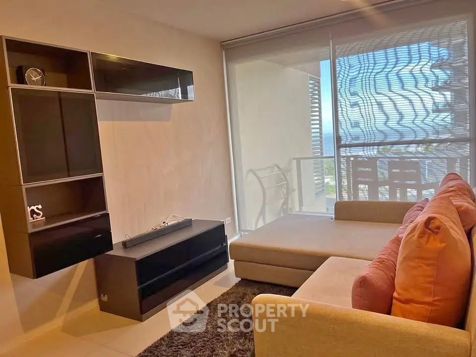 Modern living room with stylish furniture and large window offering natural light and partial balcony view.