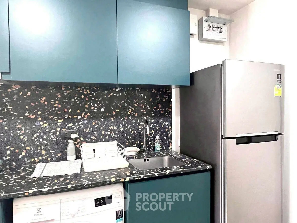 Modern kitchen with sleek cabinets, terrazzo countertop, and stainless steel fridge.