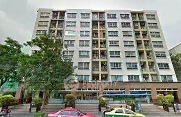 Modern multi-story apartment building with street view and lush greenery.