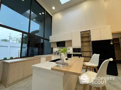 Modern kitchen with high ceilings and large windows, featuring sleek cabinetry and a central island.