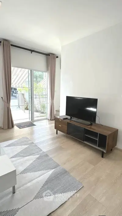 Modern living room with sleek TV stand and large window leading to balcony.