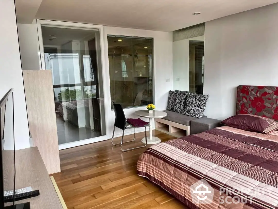 Cozy studio apartment with hardwood floors, modern furnishings, and ample natural light, featuring a comfortable bed, dining area, and access to a private balcony.