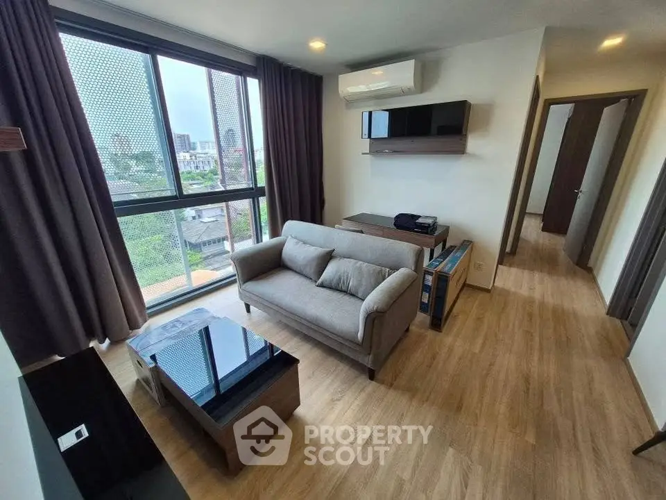 Modern living room with large window and city view, featuring sleek furniture and wooden flooring.