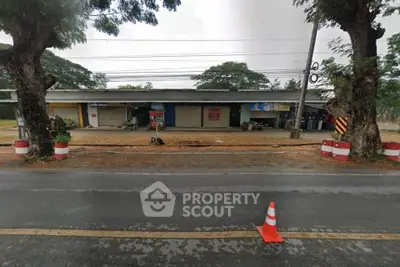 Street view of commercial building with closed shutters and trees lining the road.
