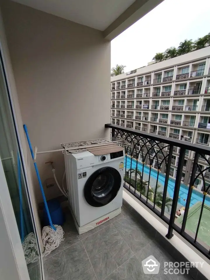 Charming balcony with washing machine overlooking modern apartment complex and pool.