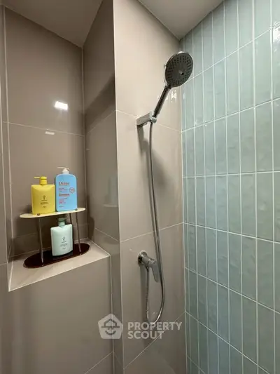 Modern bathroom shower area with sleek tiles and built-in shelf for toiletries.