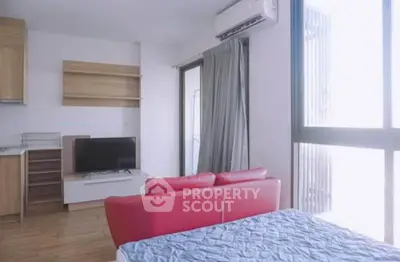 Modern studio apartment with red sofa, TV, and large windows for natural light.