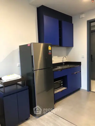 Modern kitchen with sleek blue cabinets and stainless steel fridge in compact layout.
