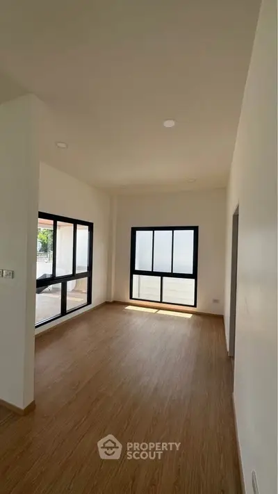 Spacious empty room with large windows and wooden flooring, perfect for customization.
