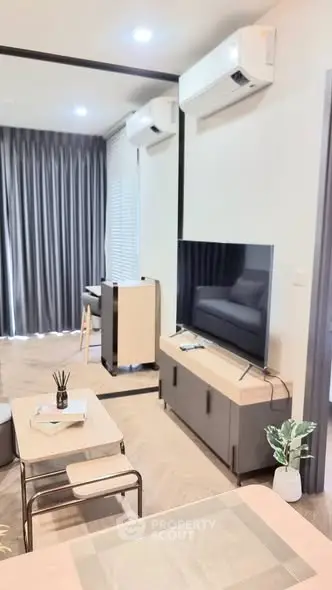 Modern living room with sleek furniture and large TV, featuring air conditioning and stylish decor.