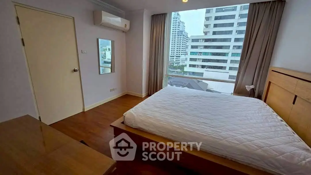 Spacious bedroom with city view and modern furnishings in high-rise apartment.