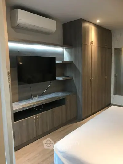 Modern bedroom with built-in wardrobe and wall-mounted TV, featuring sleek design and ample storage space.