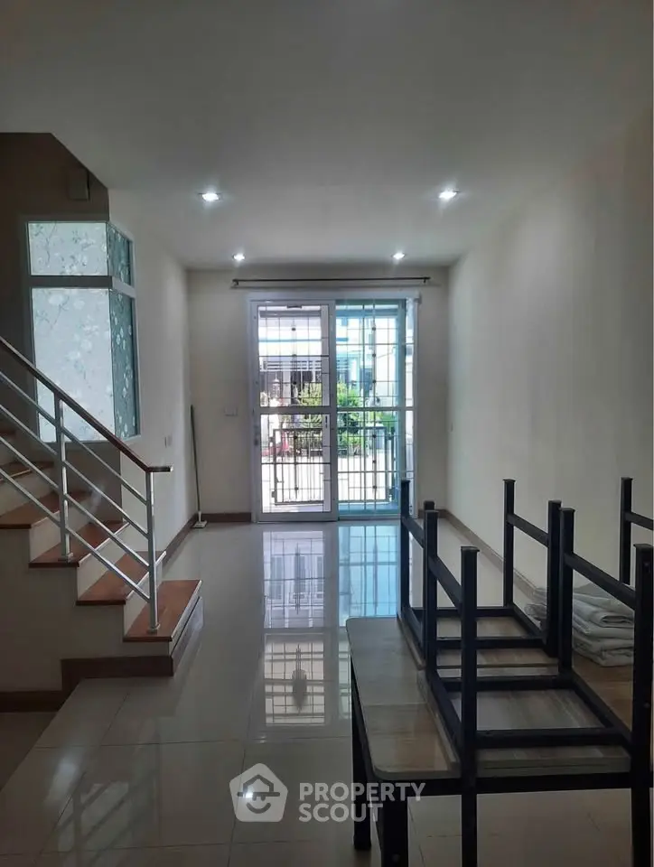 Spacious living room with modern staircase and large window opening to a balcony.