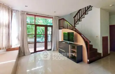Spacious living room with staircase and large windows overlooking greenery