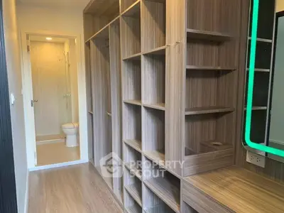 Spacious walk-in closet with modern wooden shelving and adjacent bathroom in luxury apartment.