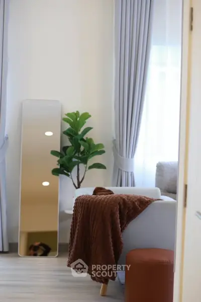Cozy living room with modern decor, featuring a full-length mirror, lush plant, and soft furnishings.