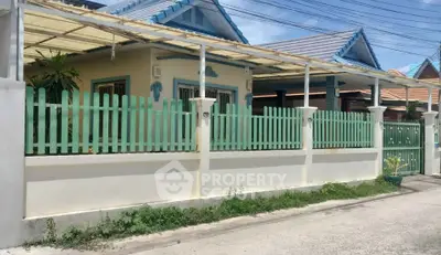 Charming single-story home with pastel picket fence and covered porch in a serene neighborhood.