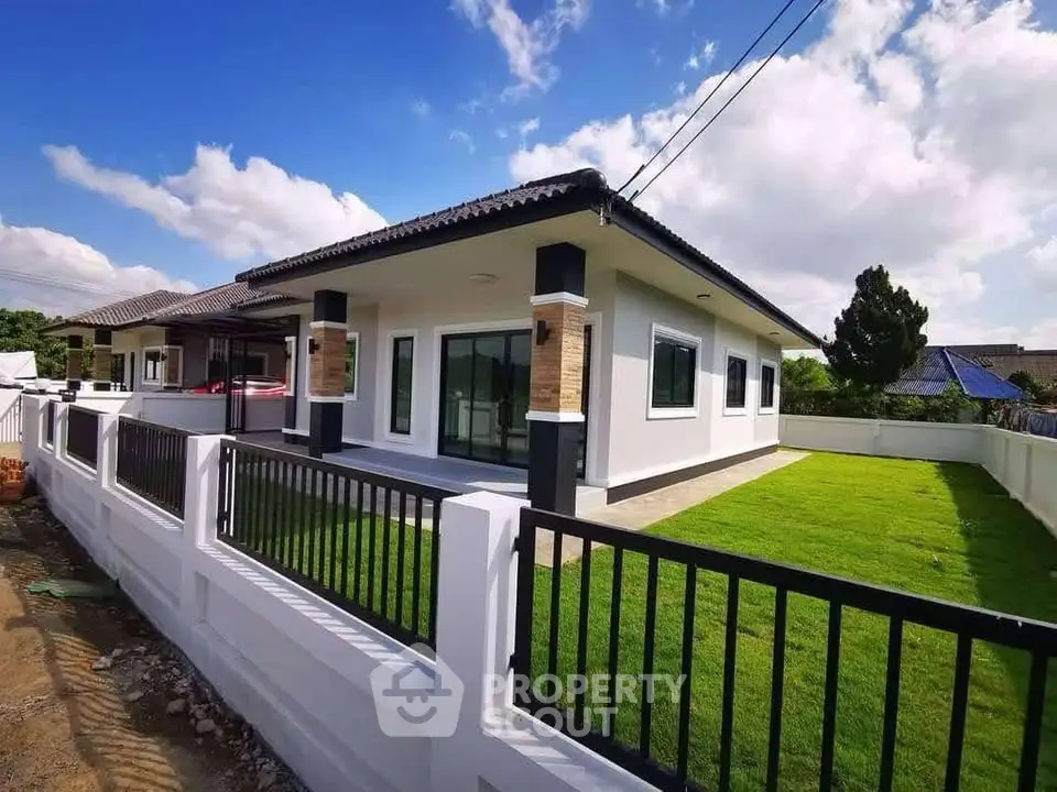 Modern single-story house with spacious lawn and stylish fence under a clear blue sky.