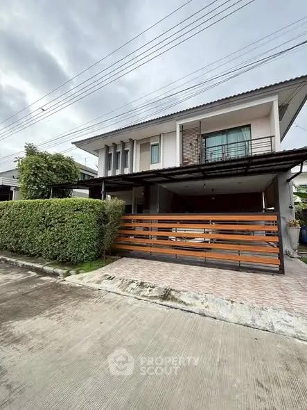 Modern two-story house with balcony and hedge, featuring a sleek wooden fence and driveway.