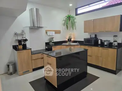 Modern kitchen with sleek black countertops and wooden cabinets, featuring an island and stainless steel appliances.