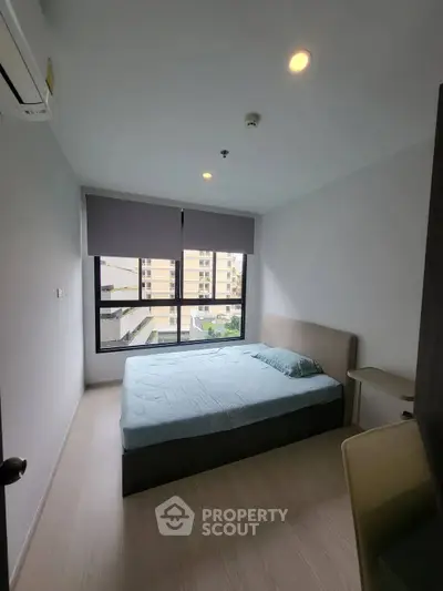 Modern bedroom with large window and minimalist decor in urban apartment.