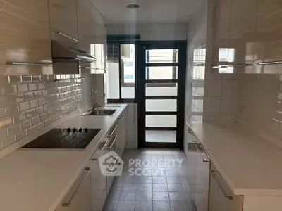 Modern kitchen with sleek cabinetry and electric cooktop in a bright, narrow layout.