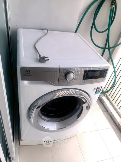 Modern Electrolux washing machine on tiled balcony with green hose.