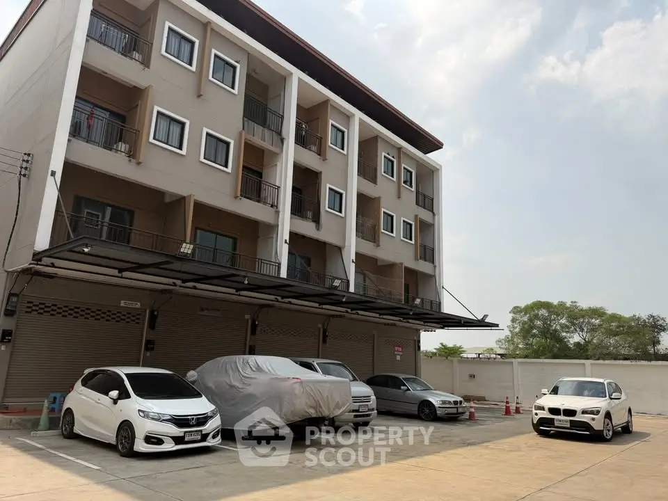 Modern multi-story building with parking area and cars, showcasing urban living convenience.