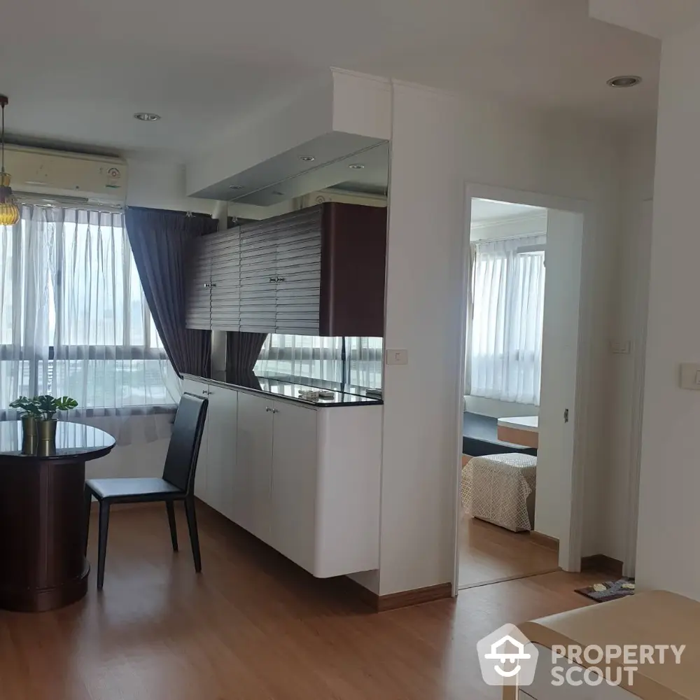 Modern apartment interior with open kitchen and dining area, featuring wooden flooring and natural light.