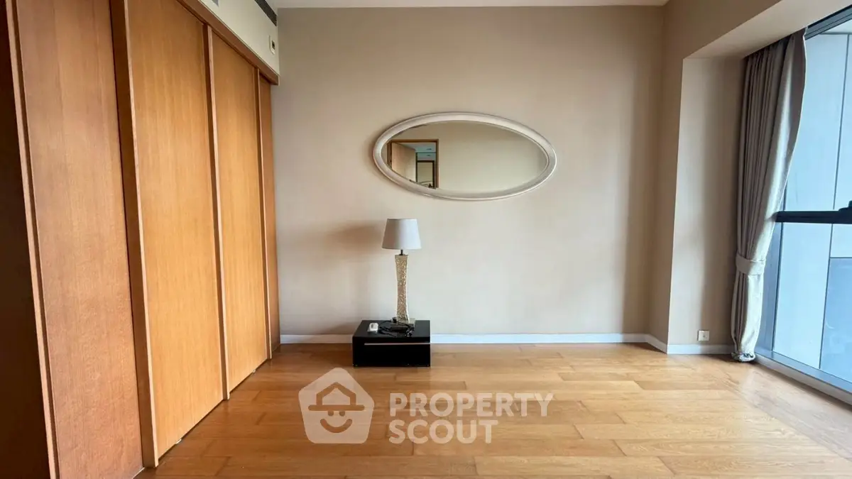 Spacious room with wooden floors, large mirror, and natural light from window.