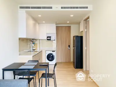 Modern studio apartment with integrated kitchen, sleek cabinetry, and full-sized appliances, including a washing machine and fridge, complemented by a cozy dining area.