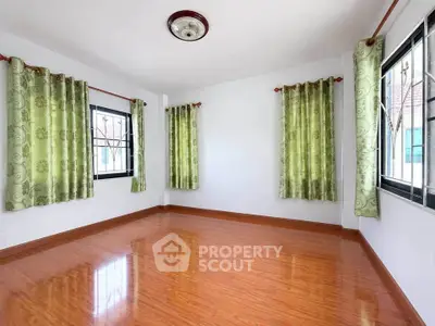 Spacious empty room with wooden flooring and green curtains, perfect for customization.