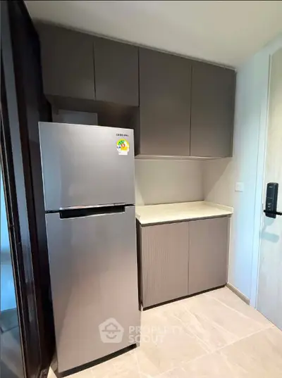 Modern kitchen with sleek cabinets and stainless steel fridge in compact layout.