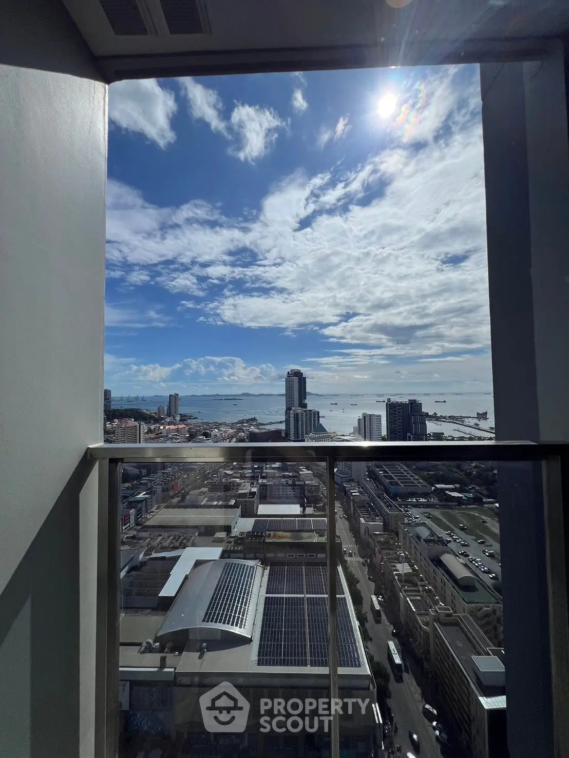 Stunning high-rise balcony view of city skyline and ocean under a bright blue sky.