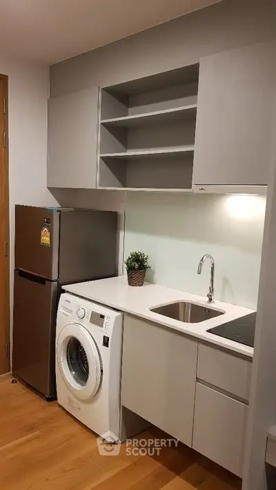 Modern kitchen with washing machine, fridge, and sleek cabinetry in compact layout.