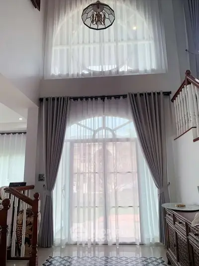 Elegant high-ceiling living room with large windows and stylish curtains