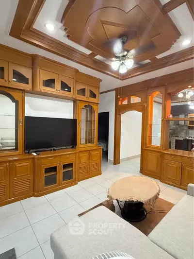 Elegant living room with wooden cabinetry and ceiling design, featuring a cozy seating area and modern TV setup.