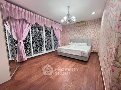 Charming bedroom with floral wallpaper and elegant chandelier, featuring hardwood floors and large windows with ornate curtains.